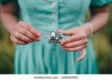 Female Hands Rotating Gears Of Old Music Box Mechanism. Lady Turning Lever Of Retro Small Metallic Carillon. Woman In Vintage Dress Listening To Music Which Playing.