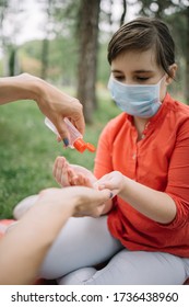 Female Hands Sanitizing Child's Hands With Disinfectant. Cropped Woman Putting Hand Sanitizer On Kid's Hands While Sitting In Forest.