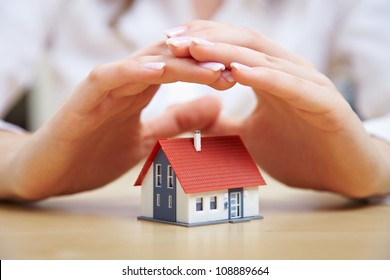 Female hands saving small house with a roof