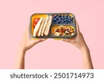 Female hands and school lunch box with blueberry on pink background