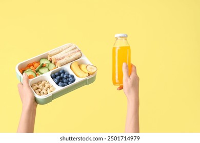 Female hands with school lunch box and  bottle of juice on yellow background - Powered by Shutterstock