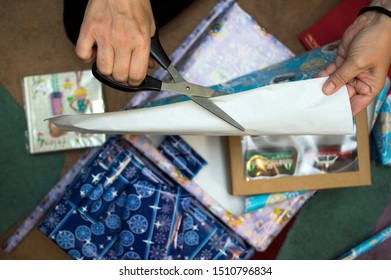 Female Hands With Scissors Cutting Wrapping Paper For Christmas Gifts, Overhead Close-up