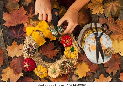 Female hands sew a textile pumpkin to decorate an autumn straw wreath on a wooden background. DIY patchwork