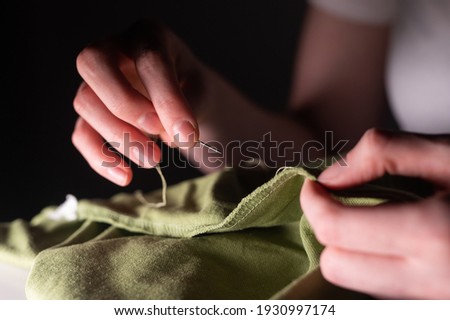 Female hands with sewing needle and thread mending clothes. Handicraft