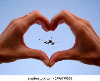 Female Hands In Shape Of Love Heart And The Airplane Flying Into The Sky. Expression Of Love For Travel.