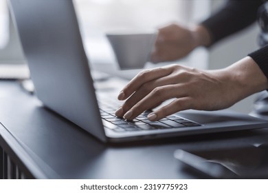 Female hands in sharp focus typing on a modern laptop keyboard, office environment in soft blur behind