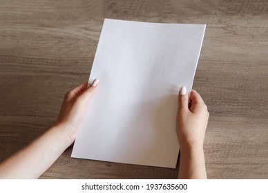 Female Hands With A Sheet Of Paper On The Background Of A Wooden Table. Mock Up