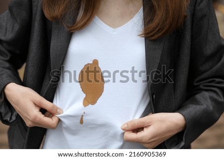 Female hands showing dirty stain of coffee on white clothes. Outodoors. The concept of cleaning stains on clothes. High quality photo
