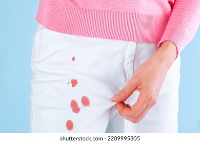 Female Hands Showing Dirty Stains On White Jeans On A Blue Background. Drops Of Blood On Clothes. Isolated. Daily Life Stain Concept. High Quality Photo