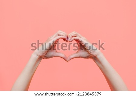 Female hands showing a heart shape isolated on a color light pink background. Sign of love, harmony, gratitude, charity. Feelings and emotions concept