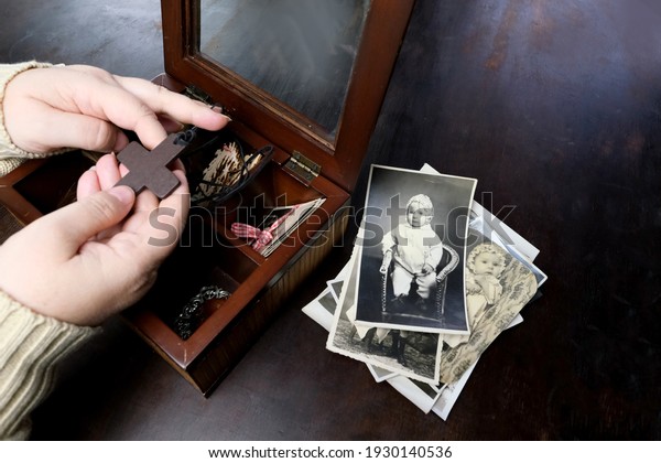 female hands sorting dear to heart memorabilia\
in old wooden box, stack of retro photographs, wooden cross,\
vintage photographs of 1960, concept of family tree, genealogy,\
childhood memories