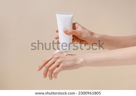 Female hands squeeze moisturizing cream from a white blank tube. Concept of cosmetology and natural skin care products. Mockup for your design.