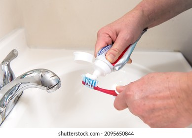 Las manos femeninas exprimen pasta dental de un tubo en un cepillo de dientes en el baño. Pincel rojo y pasta blanca.