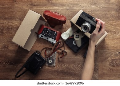 Female hands stack Retro objects in a cardboard box on a wooden floor. Antiques, vintage. Top view