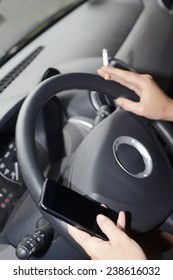 Female hands at steering wheel holding smart phone and cigarette