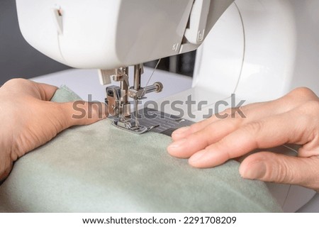 Female hands stitching white fabric on modern sewing machine at workplace in atelier. Women's hands sew pieces of fabric on a sewing machine close-up. Handmade, hobby, small business concept