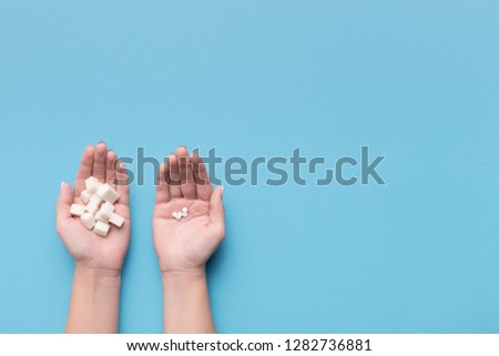 Female hands with sugar and pills on blue background. Choice of sweetener in tablets or regular sugar. Alternative to sugar for diabetics.