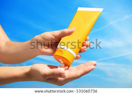 Female hands with sun protection cream on sky background. Skin care concept.