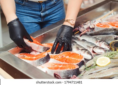 Female hands take salmon steak from showcase. Fish food at shop, close up. Raw fish ready for sale in the supermarket. Showcase with chilled red fish in grocery store. Market place with sea food.