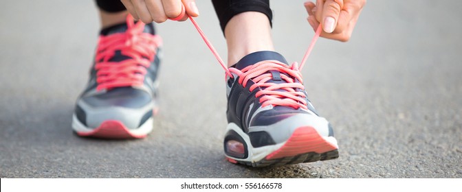 Female hands tying shoelace on running shoes before practice. Runner getting ready for training. Sport active lifestyle concept. Close-up. Horizontal photo banner for website header design