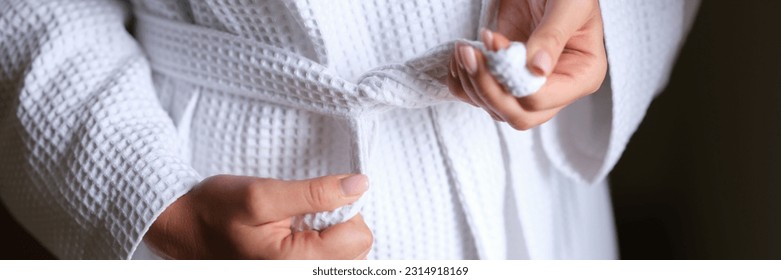 Female hands tying white bath robe closeup
