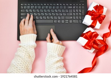 Female Hands Typing On The Keyboard Laptop Near A Gift Boxes On Pink Background. Flat Lay. Holiday Concept. Shopping.
