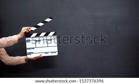 Female hands using clapperboard against black background, shooting movies