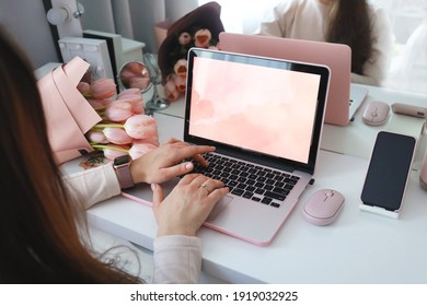 Female hands using laptop. Female office desk workspace homeoffice mock up with laptop, pink tulip flowers bouquet, smartphone and pink accessories.