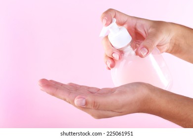 Female hands using liquid soap on pink background