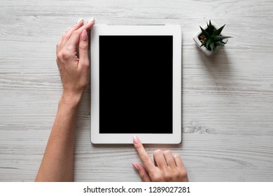 Female hands using tablet over white wooden background, overhead view. Top view, from above.