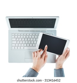 Female hands using a touch screen tablet and a laptop on white background, top view, hands close up