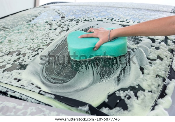 female hands washing car by using a car\
washing sponge with foam on car-wash\
station