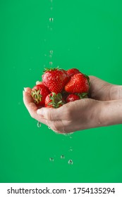 Female hands washing strawberry on the green saturated background. Concept of the importance of washing fruits under quarantine