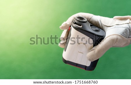 Female hands wearing professional glove with white and black modern optical range finder used for golfing or hunting.