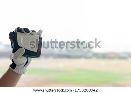Female hands wearing professional glove with white and black modern optical range finder used for golfing or hunting.