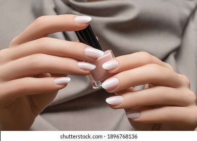 Female hands with white nail design. White glitter nail polish manicure. Woman hands on grey fabric background