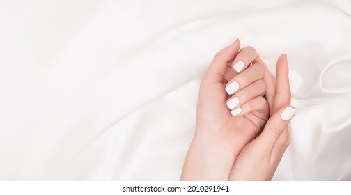 Manos femeninas con diseño de uñas blancas. Manicura de esmalte de uñas blancas. Las mujeres ponen las manos en el fondo de tela blanca. Copiar espacio. Plantilla de tema de clavos.