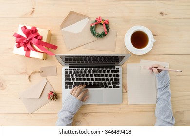 Female Hands Writing Down Wishes On Latter Paper For Christmas With Gift Box And Laptop On Desk, Top View