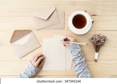 Female hands writing letter on the wooden table with cup of tea and flower