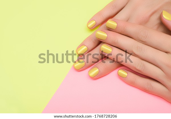 Female hands with\
yellow nail design. Yellow nail polish manicured hands. Female\
hands on yellow pink\
background