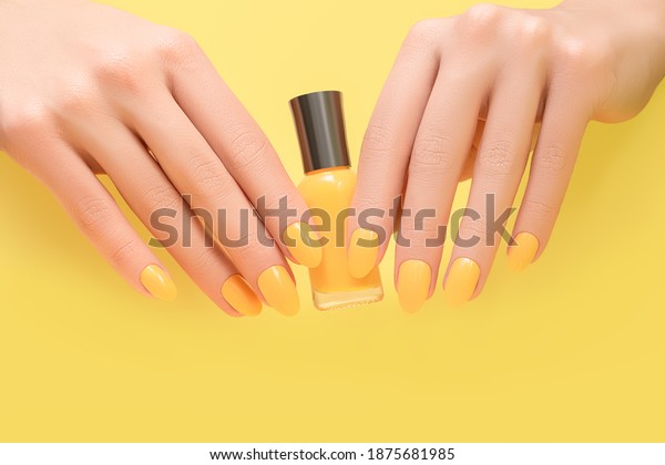 Female hands with yellow\
nail design. Female hands hold yellow nail polish bottte. Color of\
the Year 2021