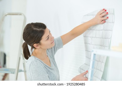 Female Handyman Applying Wallpaper At Home