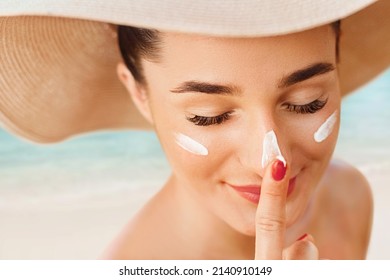 Female In Hat Applying  Moisturizing Lotion On Skin. Beautiful Young Woman With Sun Cream On Face.Skin Care. Sun Protection. Suntan