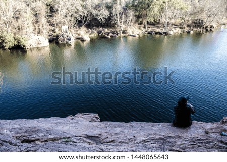 A female in a hat sitting on rocks near a beautiful river in the countryside