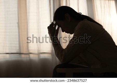 Female having depression sitting alone in bedroom dark corner. woman headache unhappy emotion. young anxiety despairing mental health problems. Dark Tone.