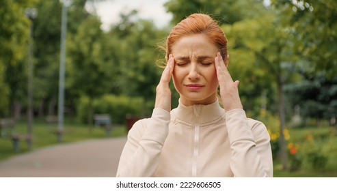 Female having a headache while jogging. Woman stops running because a head pain. Severe migraine concept. Emotions of strong suffering. Pills prescription, fitness training health problems.