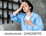 Female having heart, asthma or panic attack. Difficulties with breathe, feeling severe pain. Woman sitting on sofa with closed eyes at home and holding hands on chest and forehead.