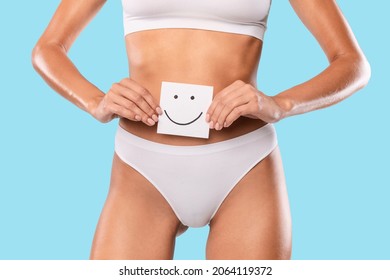 Female Health. Healthy Woman With Beautiful Fit Slim Body Holding White Paper Card With Happy Smiley Emoji Face In Hands Near Belly, Closeup Cropped, Blue Studio Background. Good Digestion Concept