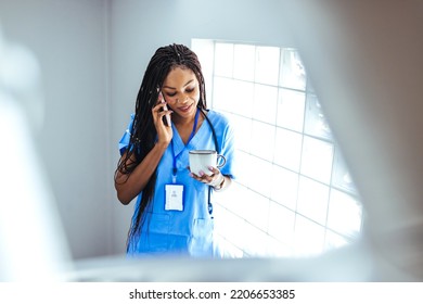 Female Healthcare Professional Talking On Her Phone As She Arrives For A Hospital Shift. She Is Wearing A Protective Face Mask. Shot Of A Female Nurse Holding A Cup Of Coffee While Using Her Cellphone