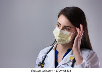 Female healthcare worker adjusting mask. Working with Coronavirus patient's in yellow PPE against a grey background - Powered by Shutterstock